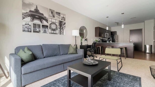Una sala de estar moderna con un sofá gris, una mesa de centro y una cocina al fondo.