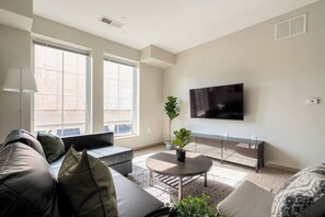 A modern living room with a sofa, a coffee table, and a flat-screen TV mounted on the wall.