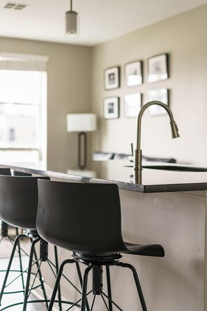 Cocina moderna con barra, que incluye un mostrador de acero inoxidable, taburetes negros y un grifo visible.