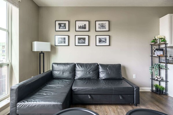 A modern living room with a black leather sectional sofa, a floor lamp, and a black shelving unit with plants.