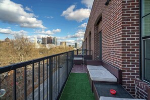 A balcony with a view of a cityscape, a brick wall, and a green artificial turf area.