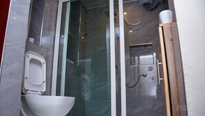 Een moderne badkamer met een douchecabine met glazen wanden, een wit toilet en een klein opbergkastje.