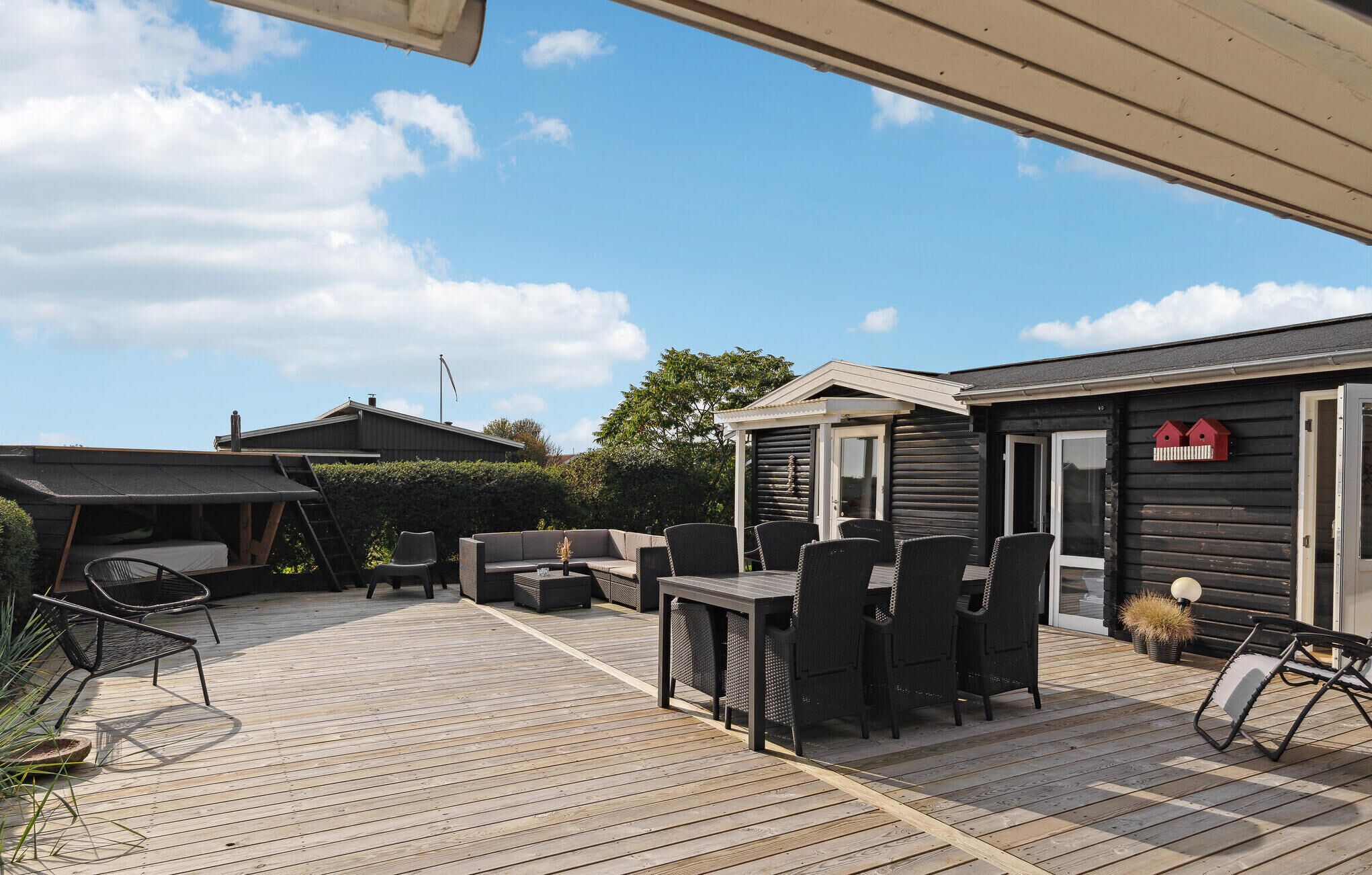 Une terrasse extérieure couverte, dotée d’une plateforme en bois, de mobilier d’extérieur et d’un petit bâtiment à l’ext érieur sombre.