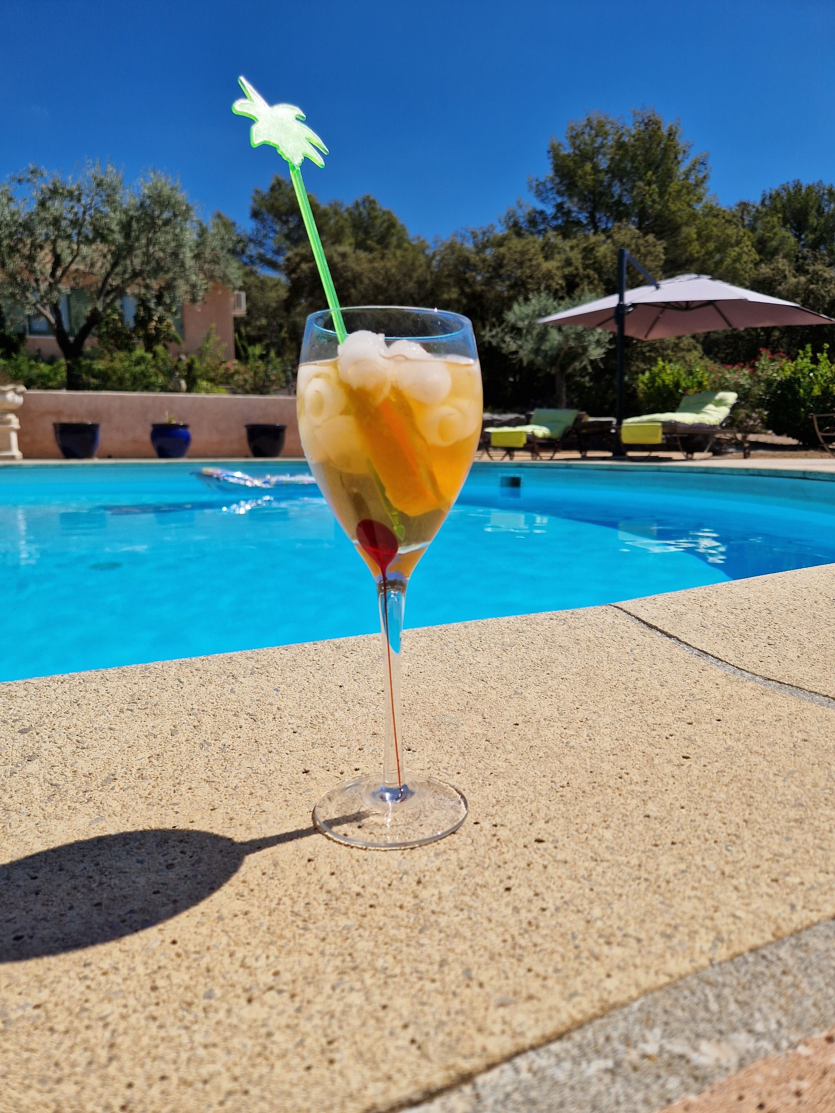 Un vaso de bebida helada con pajita y una flor decorativa junto a una piscina.