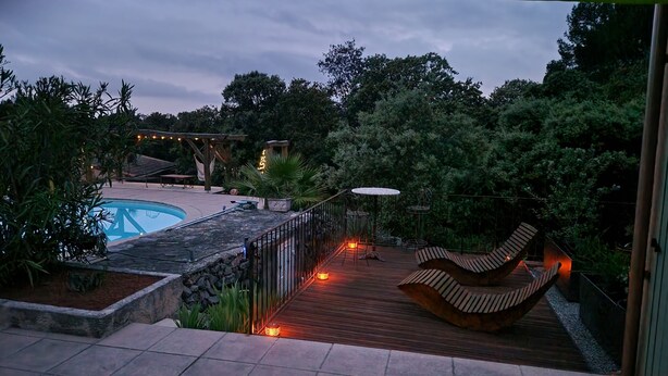 A pool area with a wooden deck, lounge chairs, and string lights.