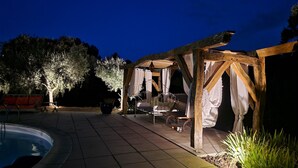 A patio area with a pool, a wooden pergola, and a seating area with a bench and a table.