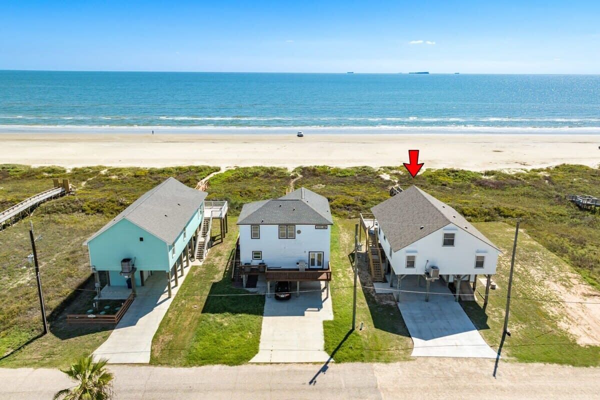 A beachfront property with three houses, a sandy beach, and the ocean in the background.