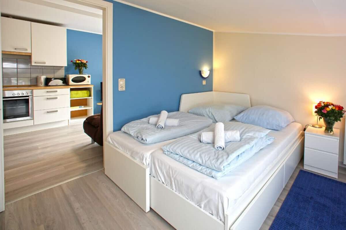 A bedroom with two beds, a kitchenette, and a bathroom.