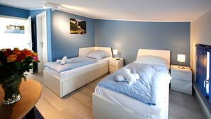 Habitación de hotel con dos camas, una mesita con un florero y una puerta que da a un balcón.