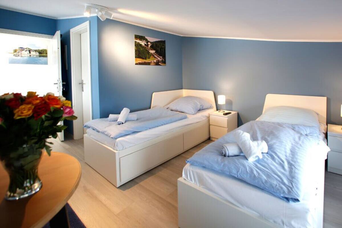 A hotel room with two beds, a small table with a vase of flowers, and a door leading to a balcony.