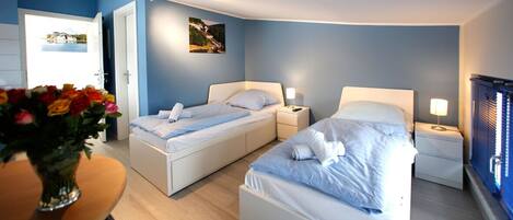 Een hotelkamer met twee bedden, een tafeltje met een bloevas en een deur naar een balkon.