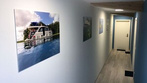 Un pasillo con un cuadro grande enmarcado de un barco en el agua, una puerta y un cuadro pequeño en la pared.