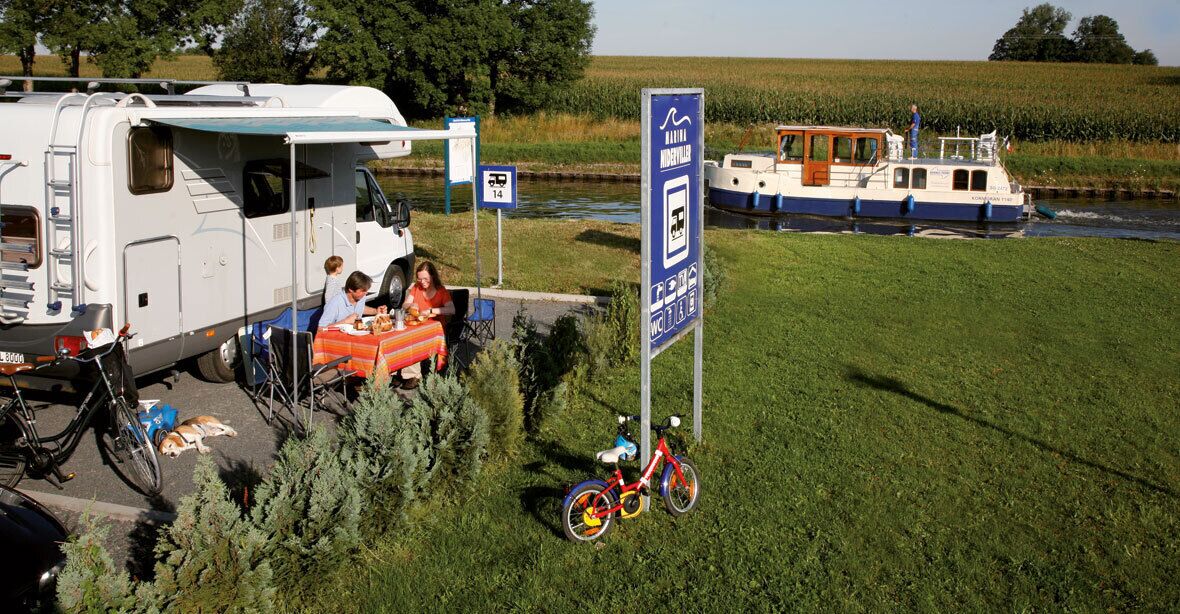 Un camping con una caravana, una bicicleta y una barca en un río.