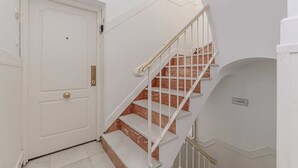 A white door with a brass handle, a white staircase with marble steps, and a white wall with a small plaque. - Recaredo, Nº3- Apartment 2 bedrooms 2nd Floor (Sevilla)