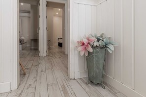 Un pasillo con paredes blancas y suelo de madera, que conduce a una habitación con cama y baño.