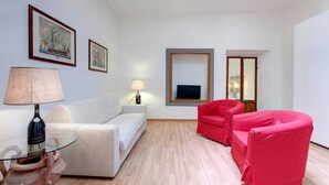 A modern living room with a white sofa, a red armchair, a glass coffee table, and a TV on the wall. - Apartment in Oltrarno area (Florence)