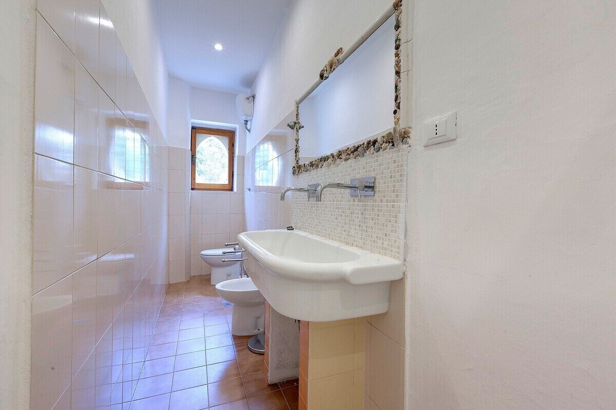 A bathroom with a white bathtub, a white sink, and a white toilet. There is a window with a wooden frame and a mirror with a decorative border.
