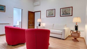 A living room with a white sofa, two red armchairs, a glass coffee table, and two wall-mounted lamps. - Apartment in Oltrarno area (Florence)