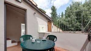 A patio with a round table and chairs, a small sink, and a window overlooking a garden. - Apartment in Oltrarno area (Florence)