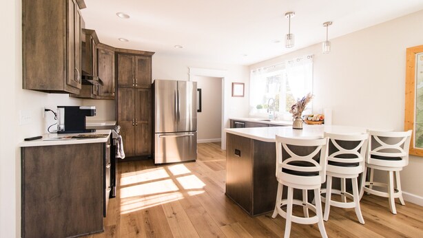 Une cuisine moderne avec des meubles en bois, des appareils électroménagers en acier inoxydable et un îlot central doté de tabourets de bar.