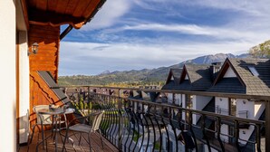 A wooden deck with a table and chairs, overlooking a mountainous landscape.