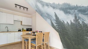 A modern kitchen with white cabinets, a wooden dining table with chairs, and a large scenic mural of a forested mountain.