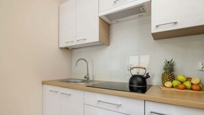 A modern kitchen with white cabinets, a stainless steel sink, and a black kettle on the countertop.