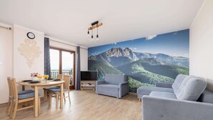 Una sala de estar moderna con comedor, sofás grises, mesa de comedor de madera y un gran mural con vistas a la montaña.