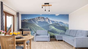 Una sala moderna con una mesa de comedor de madera, dos sofás grises y un gran mural de montañas en la pared.