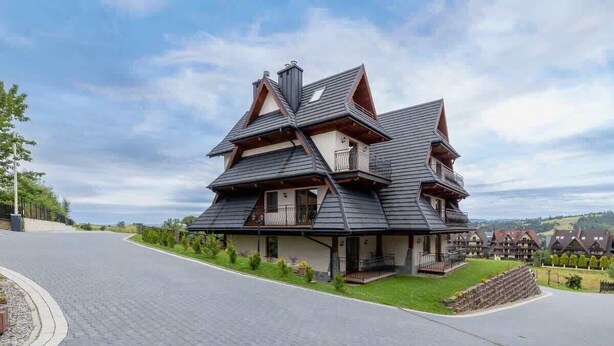 Une maison moderne à plusieurs étages, dotée d’un toit à forte pente, de grandes fenêtres et d’une pelouse bien entretenue.