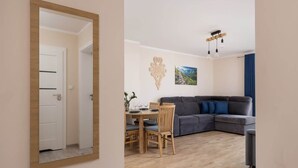 Un salon moderne avec un canapé gris, une table à manger en bois et des chaises. Un miroir sur le mur reflète la pièce.