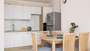 Une cuisine moderne avec des meubles blancs, un réfrigérateur gris et un coin repas comprenant des chaises en bois et une table ronde.
