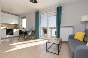 Un apartamento moderno con cocina, comedor y sala de estar. Cuenta con un balcón con cortinas, un sofá con un cojín amarillo y una mesa con sillas.