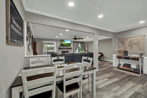 A dining area with a table and chairs, a kitchen area with a refrigerator, and a living room with a sofa and a television.