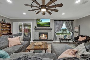Un salon avec une cheminée, un ventilateur de plafond et un téléviseur.