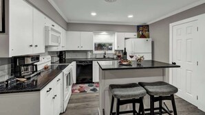 A modern kitchen with white cabinets, a black countertop, and a small bar area with stools.