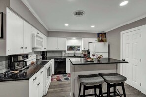 A kitchen with white cabinets, a black countertop, and a window with blinds.