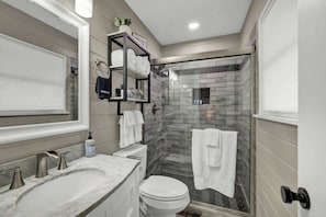 A modern bathroom with a marble sink, a toilet, a glass shower enclosure, and a towel rack.