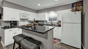 A modern kitchen with white cabinets, a central island with bar stools, a microwave, and a refrigerator.