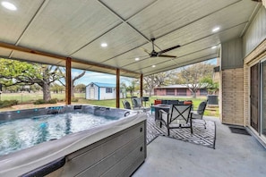 A covered patio with a hot tub, outdoor furniture, and a view of the backyard.