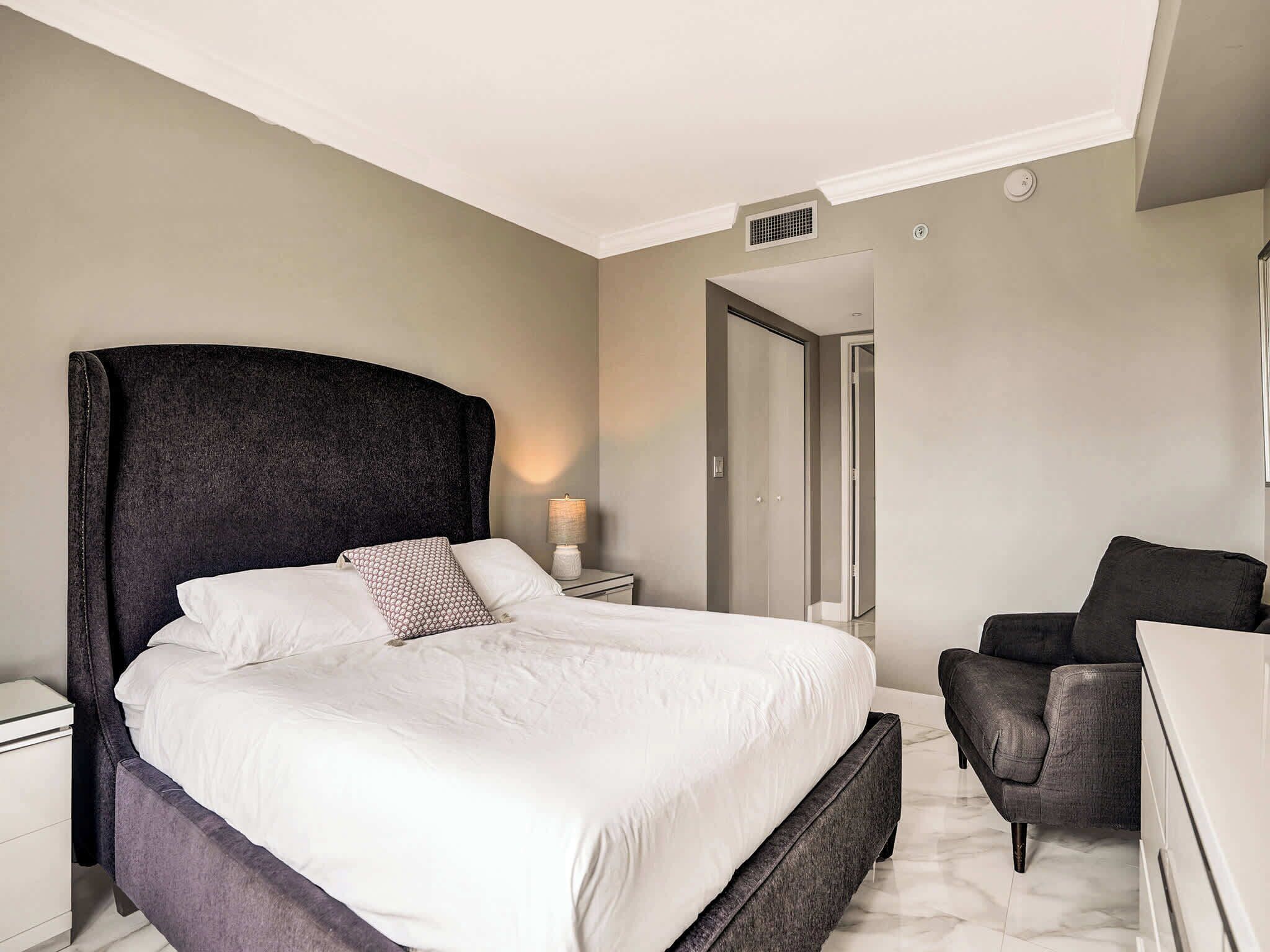 Een slaapkamer met een groot bed, een stoel, een nachtkastje en een kledingkast.