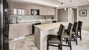 A modern kitchen with a central island, stainless steel appliances, and a marble floor.