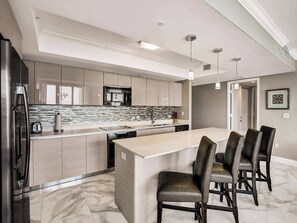 A modern kitchen with a central island, stainless steel appliances, and a marble floor.