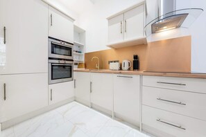 A modern kitchen with white cabinets, a double oven, a coffee maker, and a glass-fronted range hood.