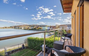 Een balkon met rieten meubilair met uitzicht op een rustig meer en een dorp.