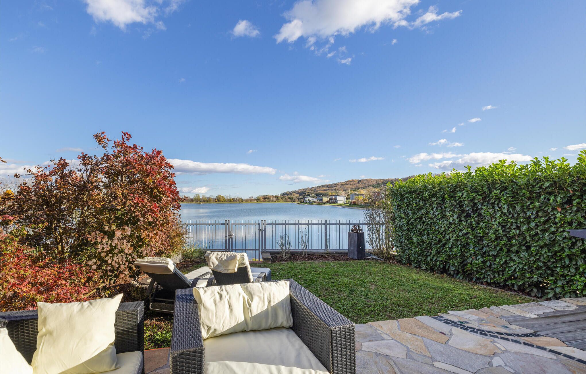 Une terrasse avec des meubles d’extérieur, un chemin de pierre et une vue sur un lac, avec des maisons en arrière-plan.
