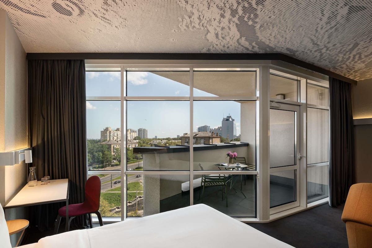 Ein Hotelzimmer mit einer großen Schiebeglaswand, einem Bett, einem Schreibtisch und einem Sessel.