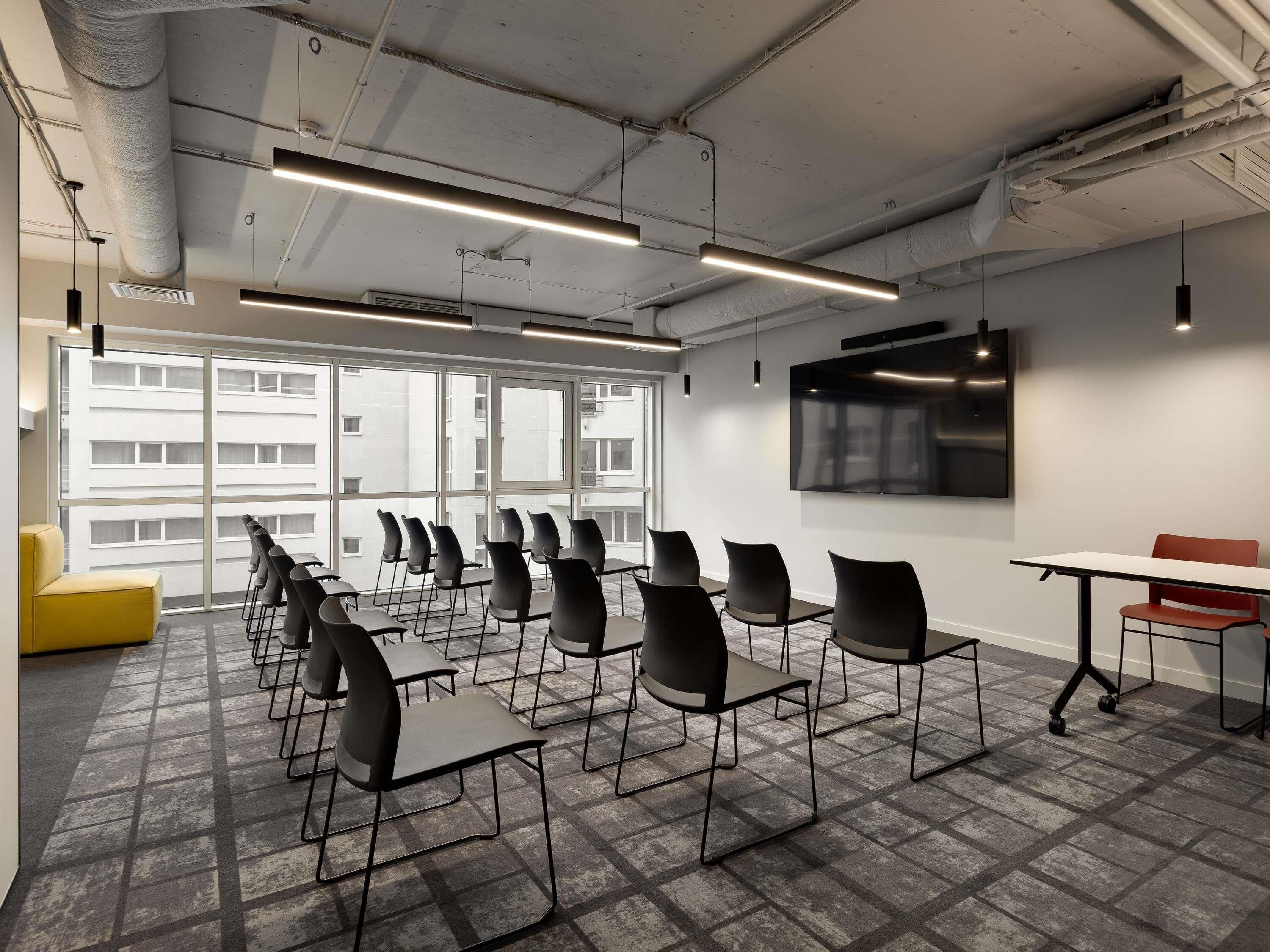 A conference room with a long table, multiple chairs, a TV screen, and large windows.