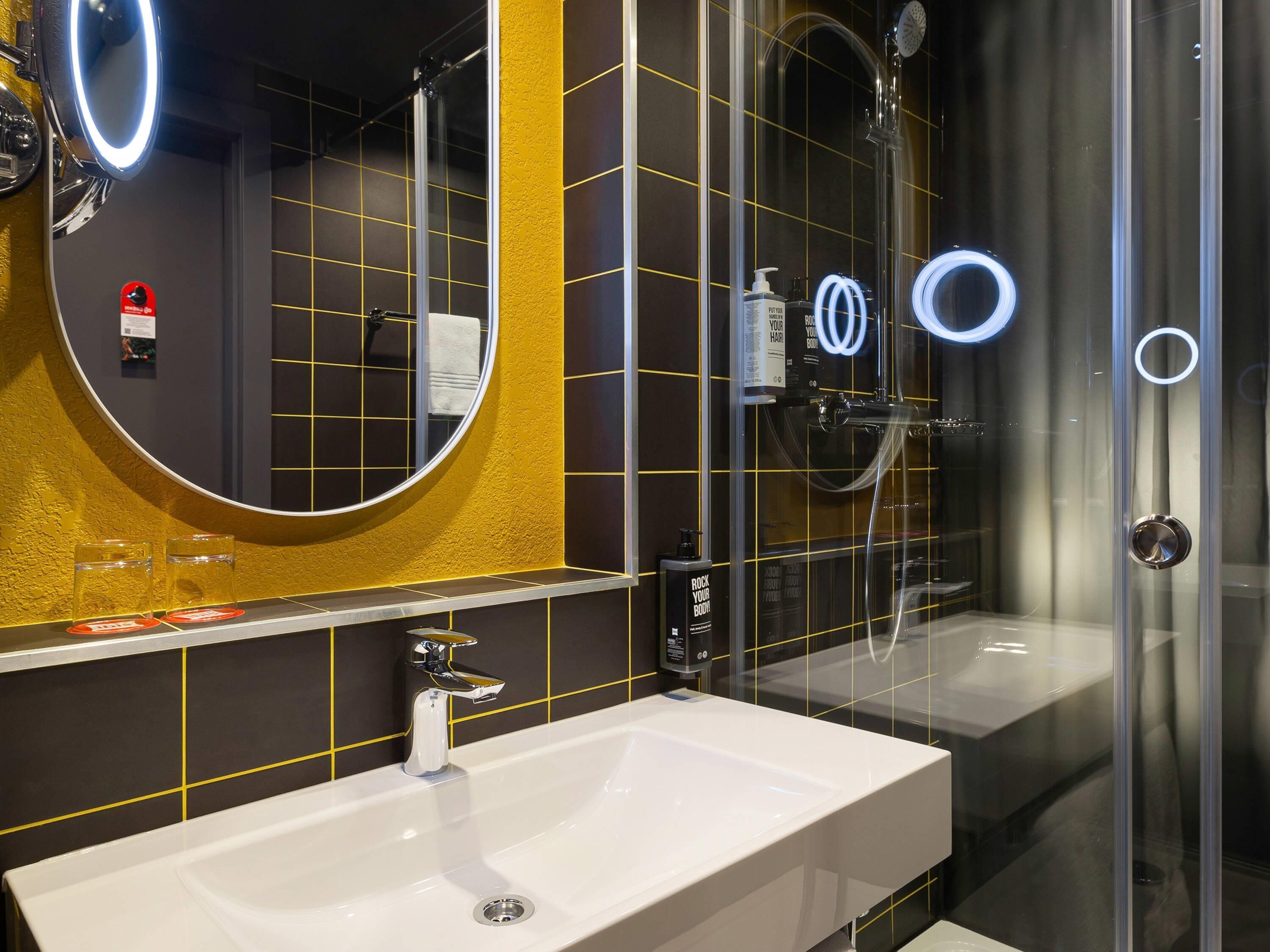 Een moderne badkamer met een grote spiegel, een witte wastafel en een douche met glazen wanden.