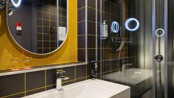 Un baño moderno con un espejo grande, un lavabo blanco y una ducha con mampara de vidrio.